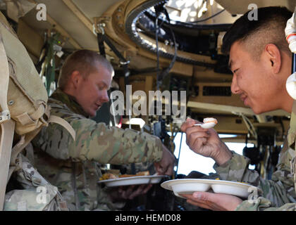 Armee Spc. Peter Chang (rechts) und US Army Spc. Zach Whiteman (links), Mitglieder der persönlichen Sicherheit Detail vom Hauptsitz und zentrale Batterie, 3. Bataillon, 320th Field Artillery Regiment, 101st Airborne Division (Air Assault), Essen Weihnachtsessen MaxxPro Mine Resistant Ambush Protected Fahrzeuginnenraum bei Combat Outpost Gerechtigkeit, Afghanistan, 25. Dezember 2012. Im Detail wurde außerhalb der Esszimmer Einrichtung veröffentlicht, während US Army Major General Clarence Chinn, stellvertretender Kommandant, Regional Command East mit Soldaten der US-Armee und afghanische Uniformierte Polizei während des Essens Urlaub besucht. (U.S. A Stockfoto