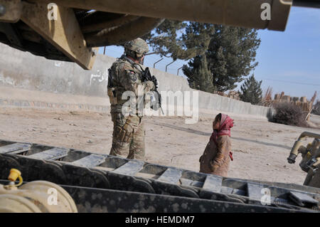 Ein afghanischer Junge Uhren Mississippi Army National Guard Mitglied Sgt.1st Klasse John Wright, 44, aus Little Rock, Frl., wie er Sicherheit außerhalb der Qalat-Baumschule in Qalat, Afghanistan, 20. Januar 2013 behauptet. Wright ist, dass die Sicherheitskräfte Zug-Sergeant für Zabul Agricultural Development Team. Drei Tage lang durchgeführt die Mississippi ADT tierärztlichen Ausbildung in Qalat-Gärtnerei, eine Erweiterung Anlage gepflegt durch die afghanische Regierung Direktion der Bewässerung, Landwirtschaft und Viehzucht. Seit seiner Ankunft in Afghanistan im September 2012, hat der Mississippi ADT mit DAIL, Prov gearbeitet. Stockfoto