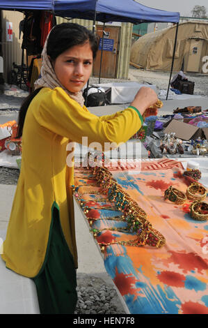 Ein afghanisches Mädchen hält die Kamera inne, als sie bejeweled Schmuck auf den afghanischen Frauen Basar, auf den afghanischen Frauen Basar, neue Compound Kabul, Afghanistan, am 23. Oktober 2013 einrichtet. Die afghanischen Frauen und Kinder ans NKC zu Hause gesponnen Kunsthandwerk verkaufen, und der Basar ist eine Chance für die Frauen und Kinder zur Unterstützung ihrer Familien durch den Verkauf von afghanischen Souvenirs. Chitter-Geschwätz von kleinen Kindern erfüllen die Luft als neue Kabul Compound, afghanische Frauen %%% E2 %%% 80 %%% 99s Basar erwacht zum Leben 131023-A-WQ129-009 Stockfoto