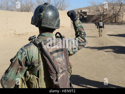 Ein Afghan National Army Special Forces Soldaten leitet die afghanische Polizei, einem nahe gelegenen Haus für Waffenlager in Mohammad Ghaws Dorf 16. Dezember 2013, in Ab Band District, Provinz Ghazni, Afghanistan zu suchen. Die Sicherheitskräfte entdeckten viele improvisierte explosive Vorrichtungen und Waffen Caches während des Betriebs. Sie fanden mehrere Pfund hausgemachte Sprengstoff, Handgranaten, ca. 200 Schuss von AK-47 Angriff Gewehrmunition und medizinische Versorgung. (Foto: US-Armee Sgt. Jared Gehmann) ANASF, ALP reduzieren Waffen, explosive Caches 131216-A-ZR634-202 Stockfoto