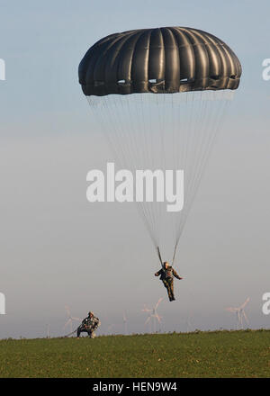 Ein deutscher Fallschirmjäger landet auf der Alzey-Drop-Zone wie ein Fallschirmjäger aus der 5. Quartiermeister Detachment (Airborne), 21. Theater Sustainment Command, am 16. Dezember aussieht. Die Fallschirmjäger wurden Betrieb Spielzeug fallen im Rahmen des internationalen springen Woche durchführen.  Die Fallschirmjäger Santa Claus eine Fahrt angeboten und lieferte er Spielzeug für Jungen und Mädchen warten bei Alzey-Drop-Zone. Betrieb Spielzeug Drop ist eine jährliche Veranstaltung, koordiniert durch die 5. Quartiermeister Distanz (Airborne), 21. Theater Sustainment Command, Spielzeug Bereich Familien anzubieten. (US Armee-Foto von Staff Sgt Warren Wright, 21. TSC öffentliche Stockfoto