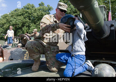 US Armee Sgt. Jeremy Carda, gebürtig aus Ogilvie, Minn, und Infanterist zugewiesen 3. kombiniert Arme Bataillon, 69. Armor Regiment, 1st Armored Brigade Combat Team, 3. Infanterie-Division, hilft eine lettische Kind Panzerhelm an eine statische Anzeige zum 25. Jahrestag der lettischen Nationalgarde in Riga, Lettland 20. August 2016 anprobieren.  Die Soldaten der 3. Mrd., 69. bestückt Rgmt., an der Veranstaltung beteiligt sind Training mit ihren baltischen Verbündeten zur Unterstützung der Operation Atlantic zu lösen, führte ein US bemüht in Osteuropa durchgeführt US-Engagement für das Kollektiv Stockfoto