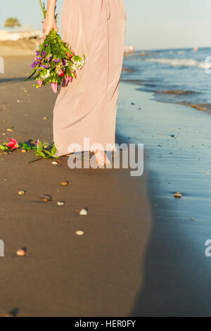 Frau mit Blumen zu Fuß am Strand entlang Stockfoto