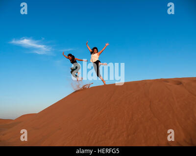 Zwei junge Frauen, die einen Sprung von Sanddüne in der Wüste, Sharqiya Sande oder Wahiba Sands, Al Raka, Oman Stockfoto