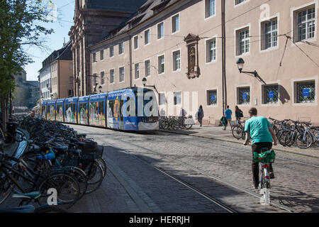 Mann Radfahren Straße mit Straßenbahn, die auf anderen Seite nähern. Geparkte Fahrräder auf dem Gehsteig. Stockfoto