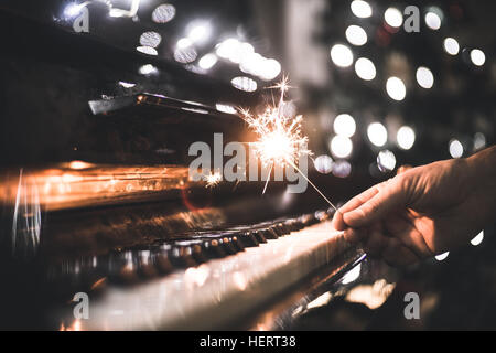 Hand hält eine Wunderkerze über ein Klavier Stockfoto