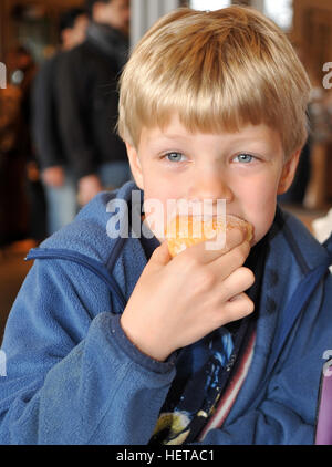 Kind Junge mit blondem Haar und blauen Augen, die einen Bissen von einem Zucker gedeckt Donut. Stockfoto