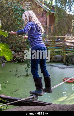 Ein junges Mädchen einen Bauernhof Teich auf einem Drahtseil zu überqueren. Stockfoto