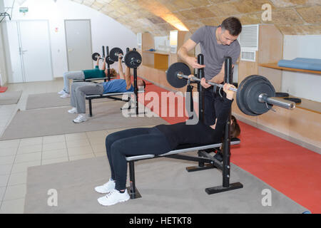 männlichen Personaltrainer helfen, junge Frau mit Hantel heben Stockfoto