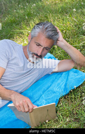 Mann Lyingsitting in den Rasen, ein Buch zu lesen Stockfoto