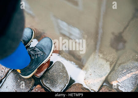 Weibliche Beine in trendigen Stiefeln auf Kopfsteinpflaster, Gebäude Reflexion über die Pfütze Oberfläche Stockfoto