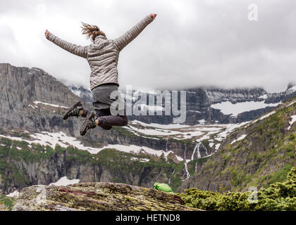 Frau in warme Kleidung springt in Aufregung mit Blick auf Berge von Montana Stockfoto