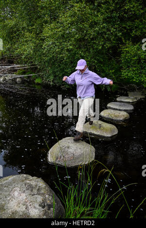 Frau ging Trittsteine über den Fluss Dee, Dumfries & Galloway, Schottland Stockfoto