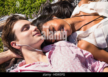 Junges Paar im Freien entspannen, auf der Decke auf dem Rasen liegen, teilen Kopfhörer Stockfoto
