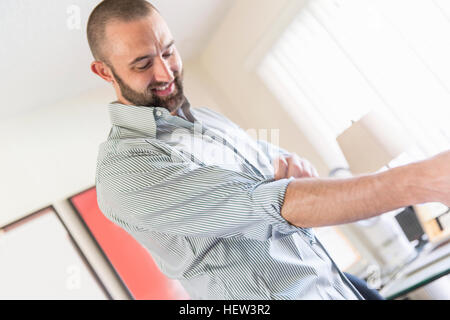 Mitte erwachsenen Mannes aufrollen Hemdsärmeln im Wohnzimmer Stockfoto