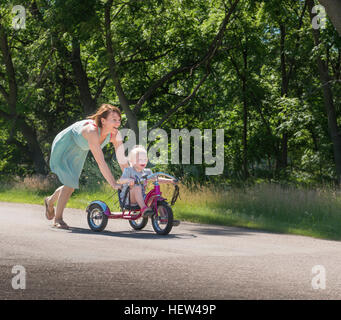 Mutter Tochter reiten Dreirad schieben Stockfoto