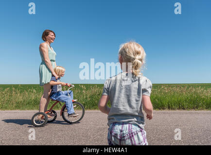 Mutter und Kinder reiten Dreirad im ländlichen Raum Stockfoto