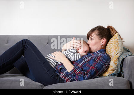 Mutter auf Sofa Babyjungen auf Stirn küssen Stockfoto