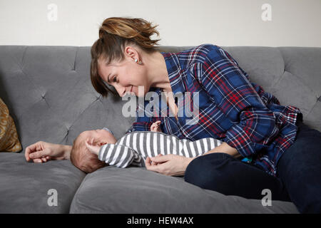 Mutter auf Sofa schlafen Baby Boy, lächelnd zu betrachten Stockfoto