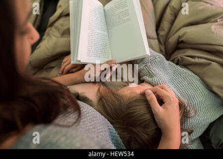 Junges Mädchen schlafend auf ihrer Mutter, während ihre Mutter ein Buch, Rückansicht liest Stockfoto