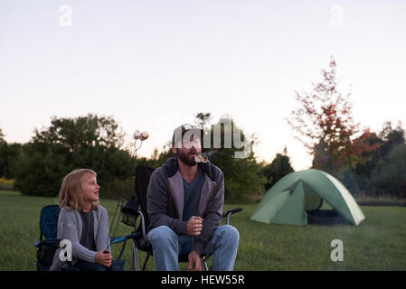 Vater und Tochter im camping Stühle, geröstete Marshmallows Essen Stockfoto