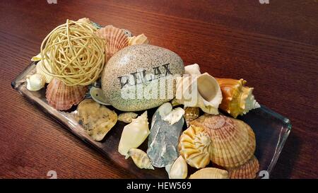 Spa-Stein mit Wort entspannen geschnitzten drauf mit Muscheln auf Holzplatte Stockfoto