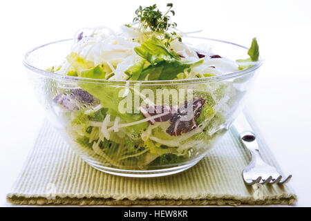 Gemischter Salat aus Weißkohl, Salat, Radicchio und Kresse in eine Glasschüssel auf einem Tischset neben einer Gabel Stockfoto