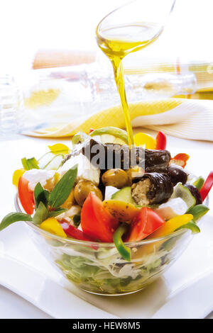 Olivenöl brütete über einen griechischen Feta Salat mit Feta-Käse gefüllte Weinstock Blätter, Weißkohl, Tomaten, Oliven Stockfoto