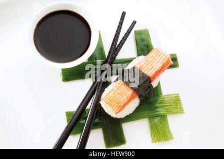 Sushi Nigiri mit Nachahmung Krabbenfleisch und eingewickelt in Nori-Algen und platzierten neben schwarzen Stäbchen und eine Schüssel mit Reis Stockfoto