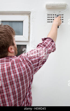 Ein Mensch malt eine Außenwand seines Hauses. Stockfoto