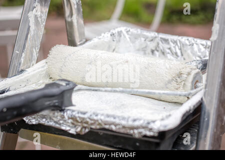 Zuletzt verwendeten Farbroller in eine Farbwanne mit weißer Farbe aufgetragen. Stockfoto