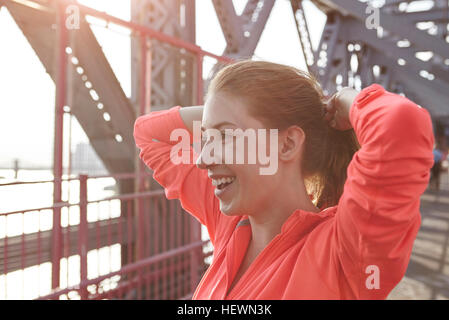 Junge Frau im Freien, die Hände hinter dem Kopf, lächelt Stockfoto
