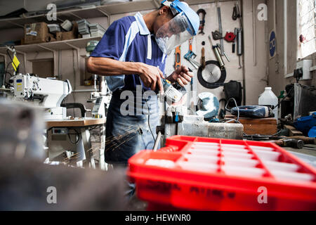 Junger Mann mit Winkelschleifer an Vize-in Reparatur-Werkstatt Stockfoto