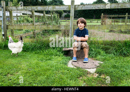 Junge sitzt auf Bauernhof mit Huhn Stockfoto