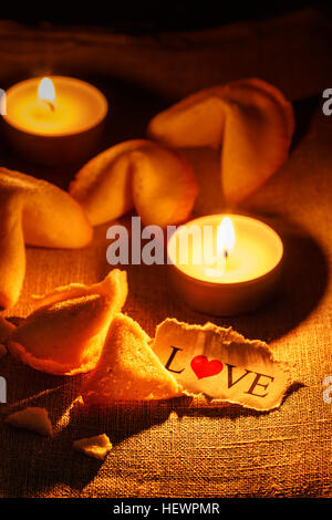 Cookies, geformt wie ein Tortellini mit das Wort Liebe auf ein Papier geschrieben und zwei Kerzen angezündet. Vertikales Bild. Stockfoto