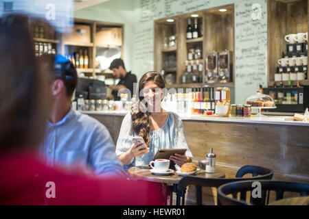 Junge Frau mit digitalen Tablet lesen Smartphone Texte im café Stockfoto