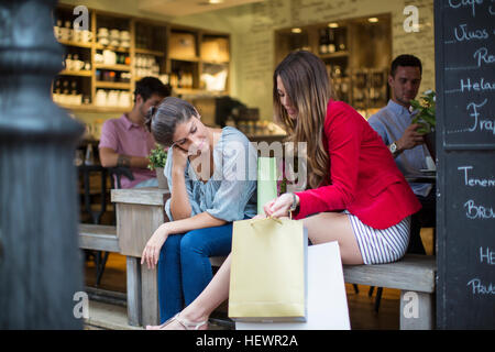 Zwei junge Freundinnen mit Einkaufstüten im Chat vor café Stockfoto