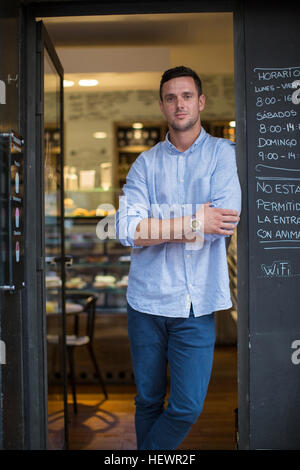 Porträt von Mitte erwachsenen männlichen Wirt Café Tür gelehnt Stockfoto
