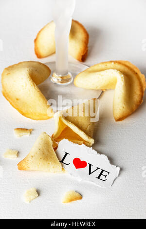 Cookies mit dem Wort Liebe geschrieben auf ein Blatt Papier und einem Glas Champagner wie Tortellini geformt. Vertikales Bild. Stockfoto