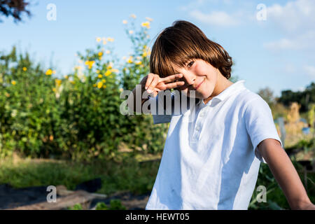 Porträt von fröhlicher Junge machen Friedenszeichen Handbewegung im ländlichen Garten Stockfoto