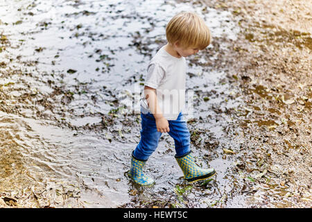 Junge Gummi Stiefel spielen in schlammigen Pfütze Stockfoto