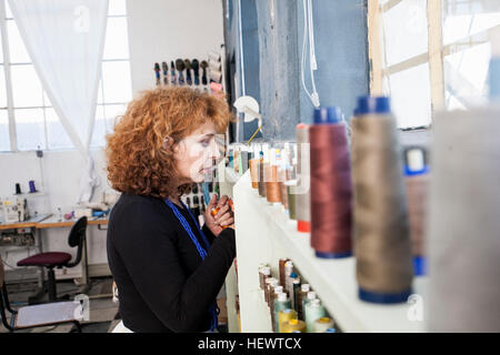 Frau in der Nähwerkstatt Regal Thread auswählen Stockfoto