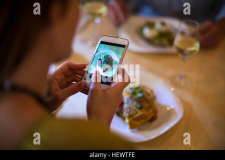 Frau nehmen Foto von ihr Essen am Tisch Stockfoto