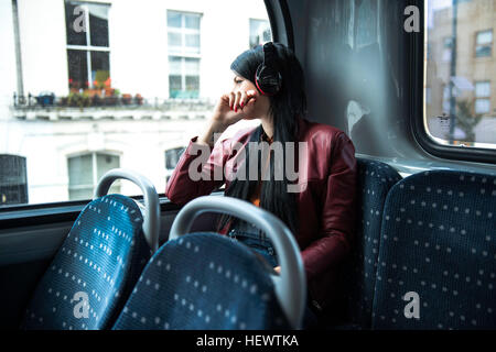 Junge Frau sitzt im Bus, tragen von Kopfhörern, Blick aus Fenster Stockfoto