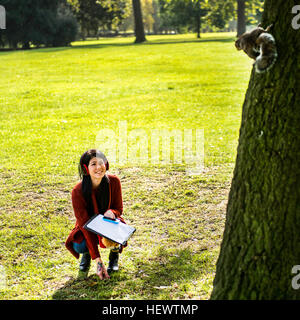 Junge Frau im Park, hockend betrachten Eichhörnchen im Baum Stockfoto