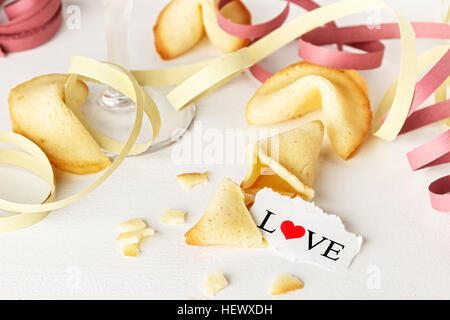 Cookies mit dem Wort Liebe auf ein Blatt Papier und ein Glas Champagner mit Streamer geschrieben wie Tortellini geformt. Horizontales Bild. Stockfoto