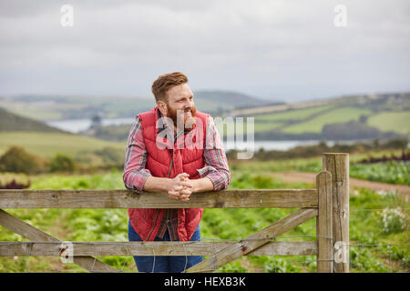 Mann auf Farm Gate wegsehen gelehnt Stockfoto