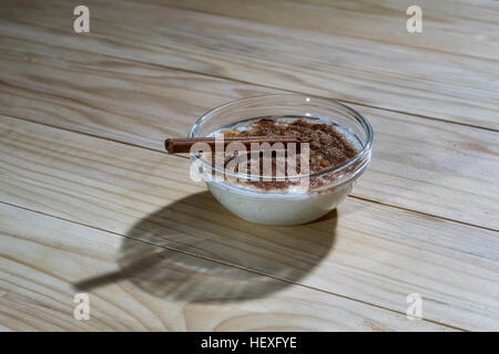 Cremiger Milchreis mit Zimtpulver und Zimtstange auf einem Holztisch Stockfoto