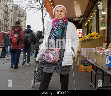 Eine ältere chinesische Frau mit einem Stock Einkaufen im Winter auf der Main Street in Chinatown, Downtown Flushing, New York City Stockfoto