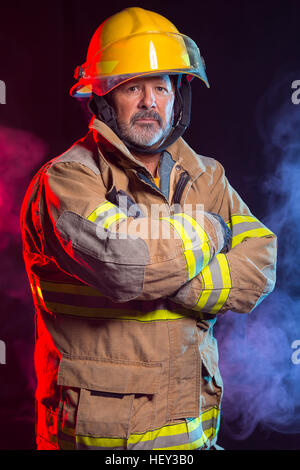 Porträt von einem Feuerwehrmann Feuerwehrmann weichen und Helm tragen. Hintergrund ist rot und blau, Rauch und Licht. Weichen sind schützen Stockfoto